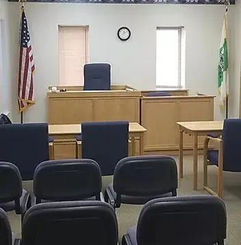 Interior view of a tribal courtroom featuring a judge's bench, wooden furniture, and rows of blue chairs, with the U.S. flag and a tribal flag displayed.