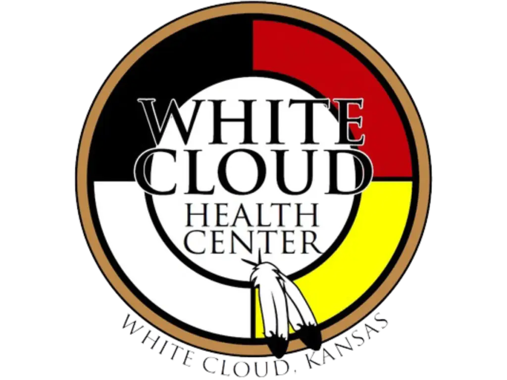 Logo of the White Cloud Health Center, featuring a medicine wheel in red, black, white, and yellow, with two feathers at the bottom and the text "White Cloud Health Center, White Cloud, Kansas."