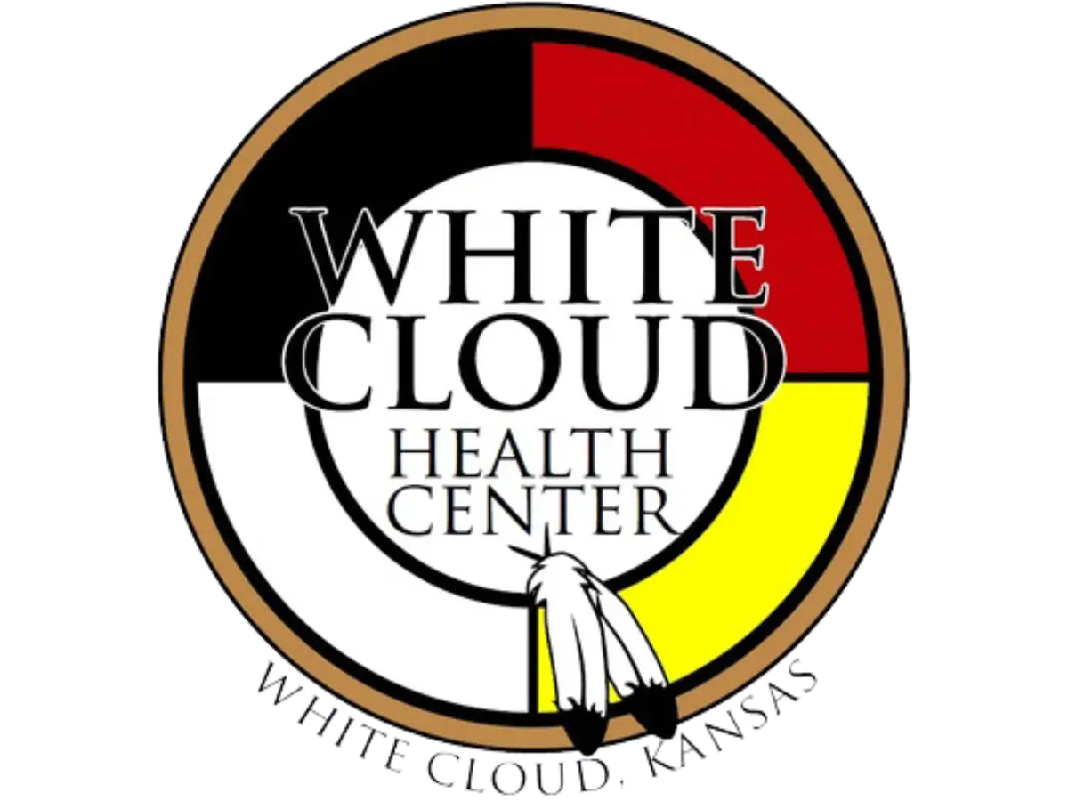 Logo of the White Cloud Health Center, featuring a medicine wheel in red, black, white, and yellow, with two feathers at the bottom and the text "White Cloud Health Center, White Cloud, Kansas."