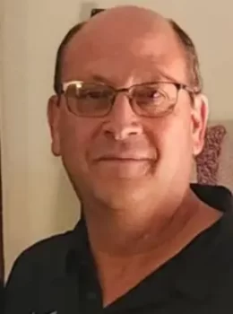 Member Bradley Campbell with glasses, wearing a black polo shirt, smiling gently at the camera.